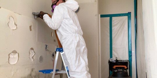 worker in protective gear on ladder using a shop vac