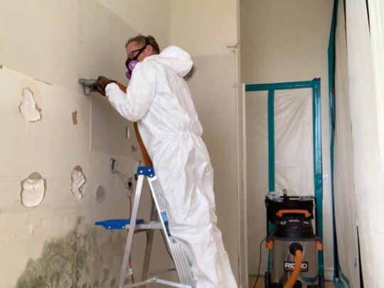 worker in protective gear on ladder using a shop vac