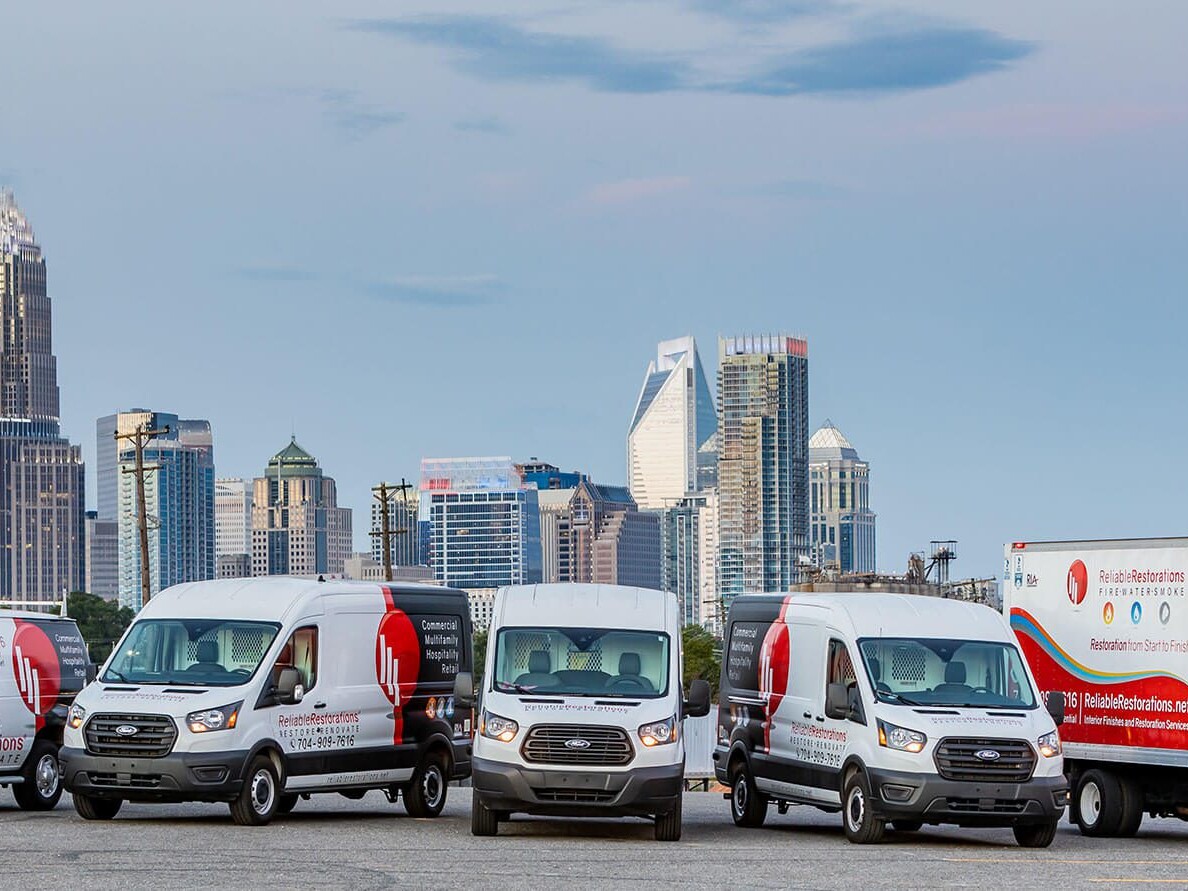 Reliable Restorations van and truck fleet in front of the Charlotte, NC skyline