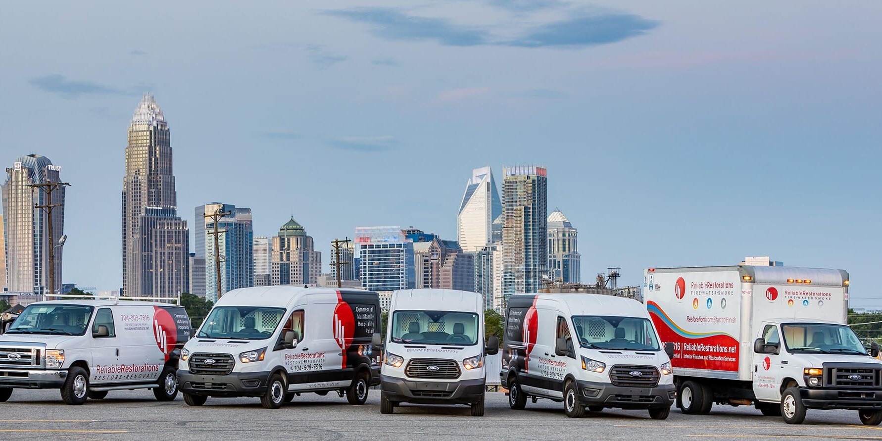 Reliable Restorations van and truck fleet in front of the Charlotte, NC skyline
