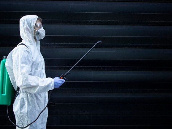 Person in white chemical protection suit holding sprayer