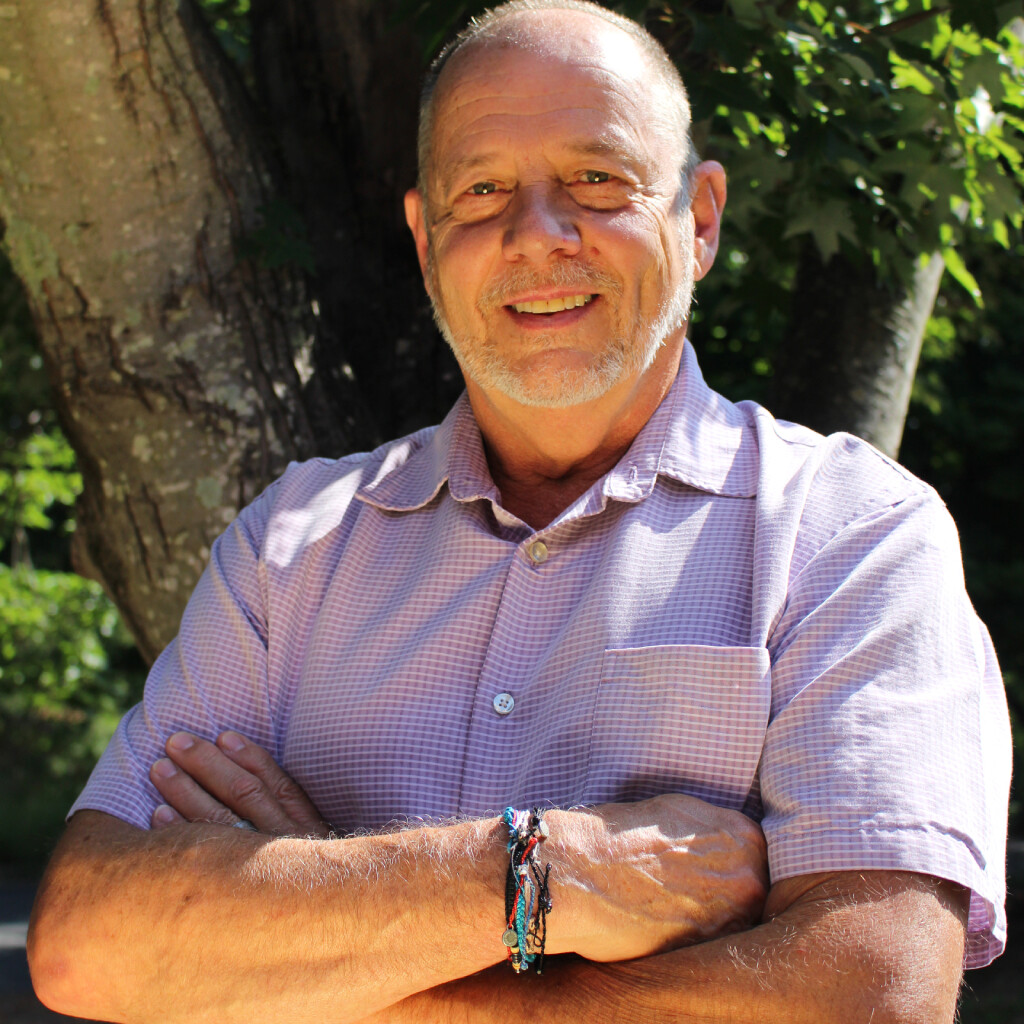 smiling older man with arms crossed in front of a tree